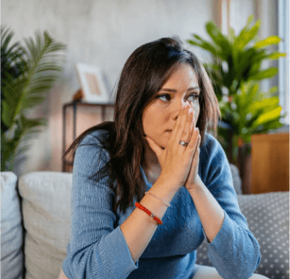 Woman sitting on a couch with her hands folded in front of her face, looking concerned