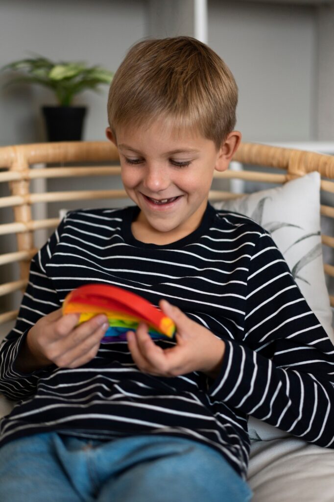 Young boy sitting in a rattan chair with a rainbow-colored toy