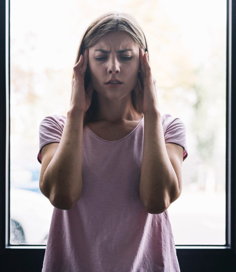 Woman holding her head in pain in front of a large window