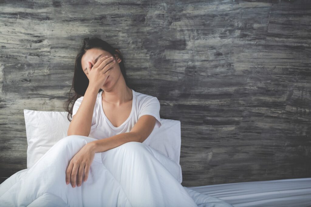 Woman sitting against her pillow in bed, hand over face